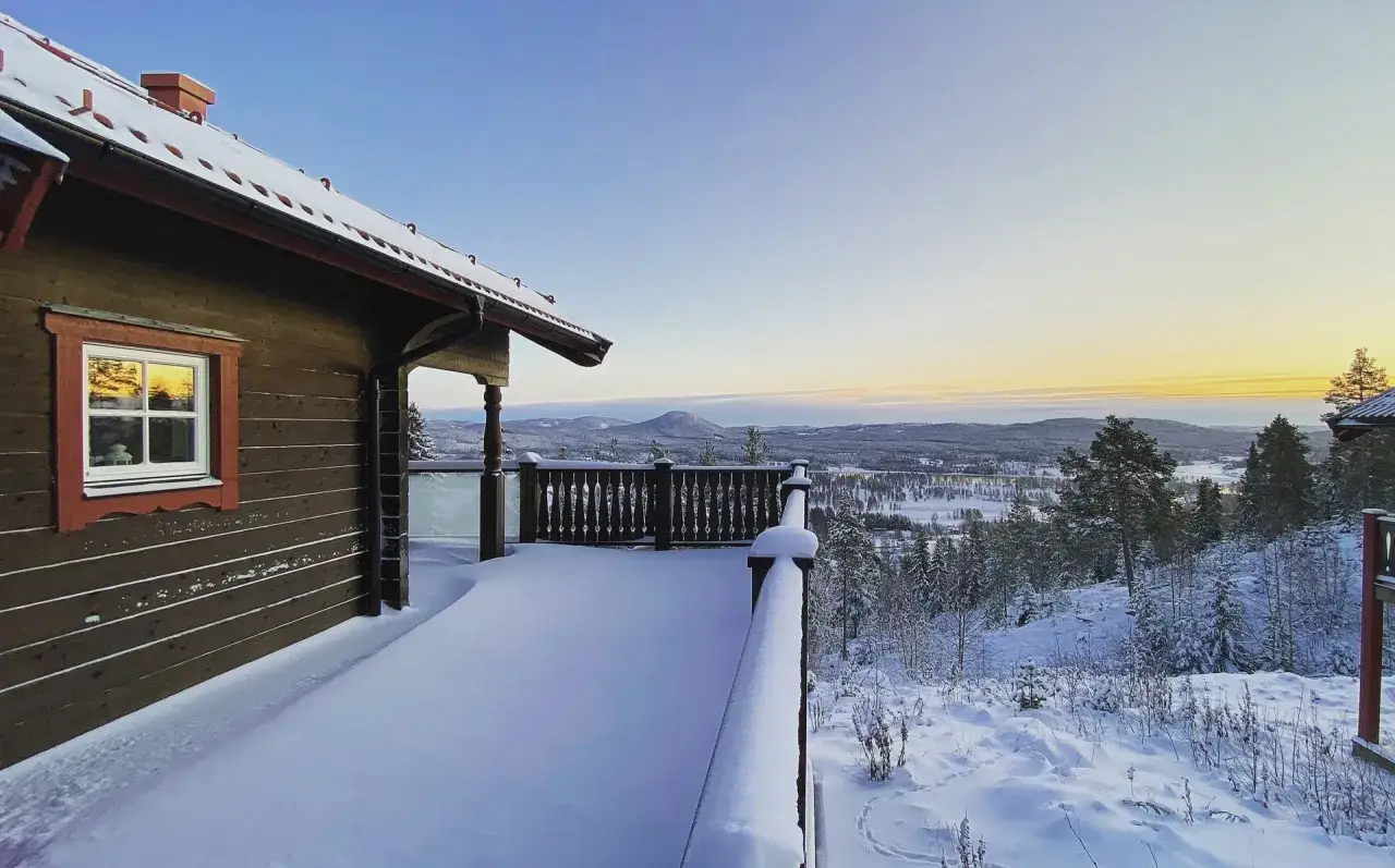 Vintervy fr&aring;n en sn&ouml;t&auml;ckt altan vid alpstigen i J&auml;rvs&ouml;. Solnedg&aring;ngen f&auml;rgar himlen &ouml;ver det sn&ouml;kl&auml;dda landskapet.