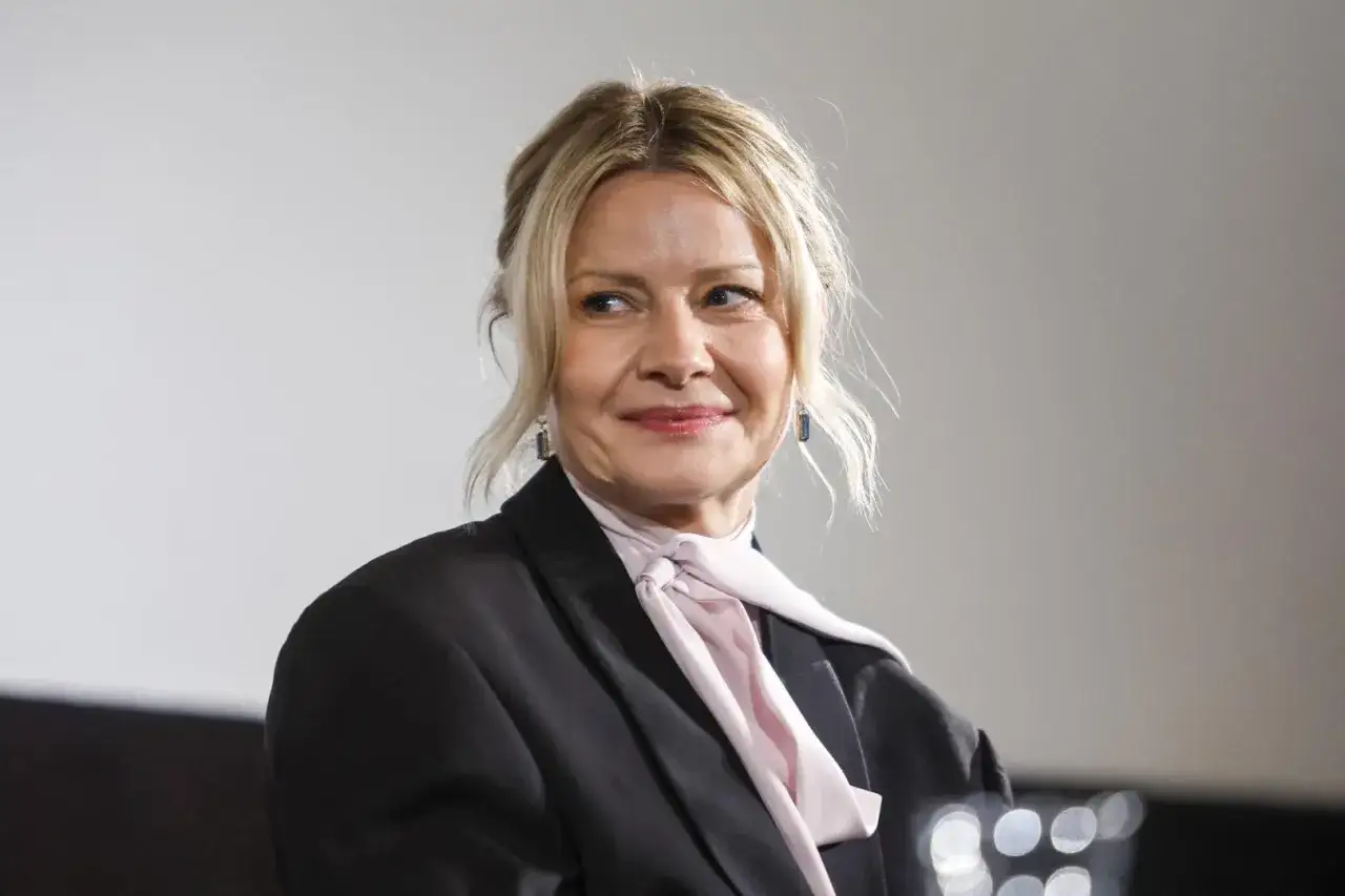 Uśmiechnięta Małgorzata Kożuchowska w czarnym żakiecie i różowej apaszce. Jej wiek dodaje jej uroku i doświadczenia.
