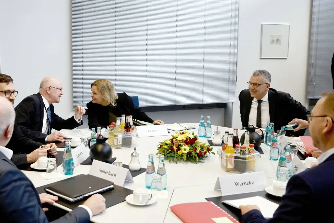 Diskussion am Tisch: Was hei&szlig;t Verdi? Eine Frau und M&auml;nner im Anzug sprechen, Getr&auml;nke und Blumen stehen bereit.