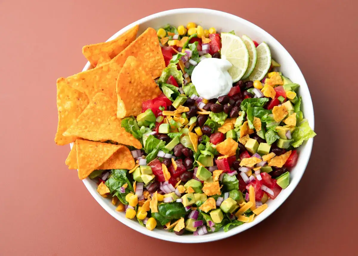 Bunter, vegetarischer Nacho Salat mit Avocado, schwarzen Bohnen, Mais, Tomaten, Zwiebeln, Käse und einem Klecks Sour Cream. Dazu knusprige Tortilla-Chips.