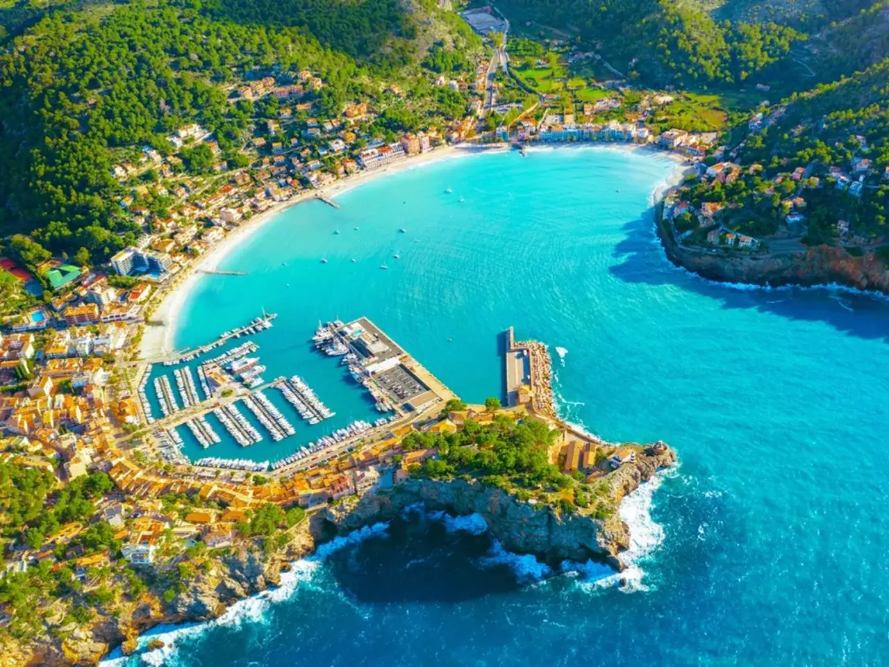 Vacker vy över Port de Sóller med turkost vatten, en strand och en livlig marina full av båtar.