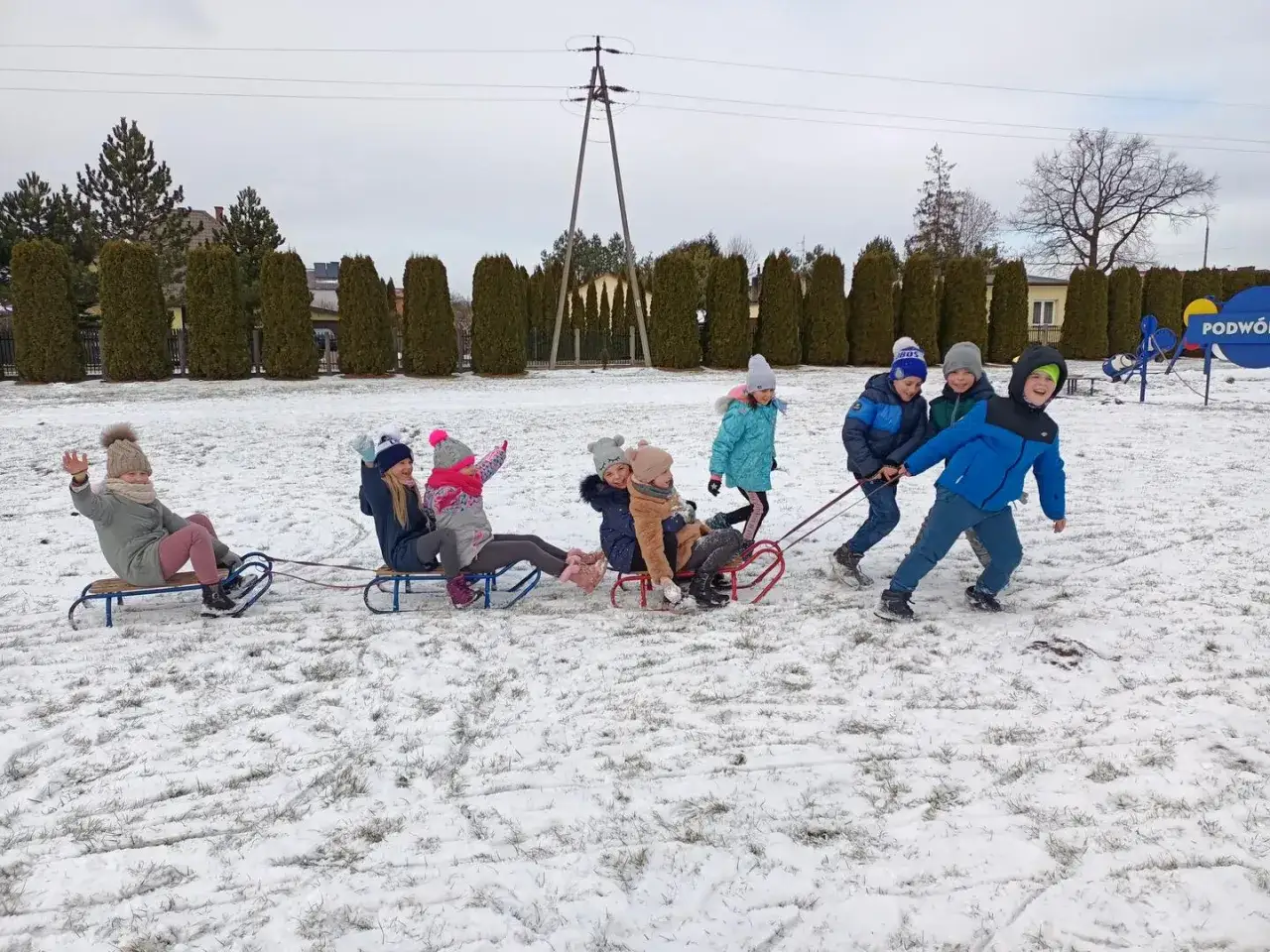 Wesołe dzieci na śniegu ciągną sanki z przyjaciółmi. Radość i zabawa na zimowym podwórku.