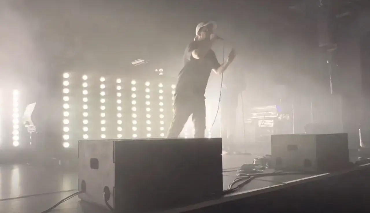 Ein Mann mit Mikrofon auf einer Bühne, umgeben von Nebel und Lichtern. Er könnte der beste deutsche Rapper sein, der gerade sein Publikum begeistert.