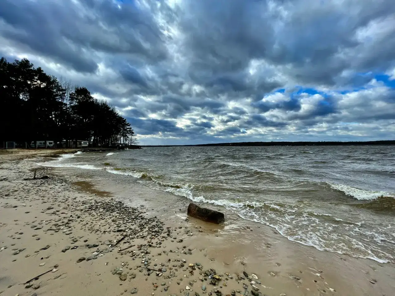 Mroczne chmury nad Zalewem Sulejowskim. Wiatr faluje wodę, a kamienista plaża zaprasza do spaceru. To miejsce oferuje wiele atrakcji.