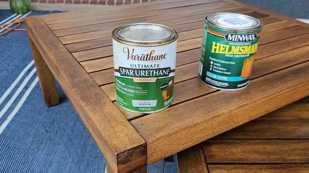Dwa puszki lakieru Spar Urethane na drewnianym stole ogrodowym. Idealne, by dowiedzieć się, jak zabezpieczyć drewno na zewnątrz.
