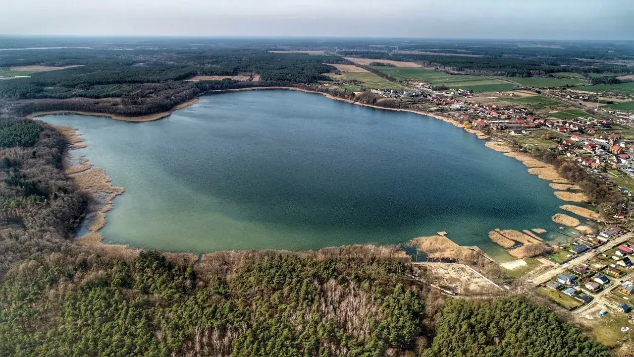 Rozległe jezioro Wilkowskie otoczone lasami i zabudowaniami. Woda ma odcień głębokiego granatu, przechodząc w turkus przy brzegu.