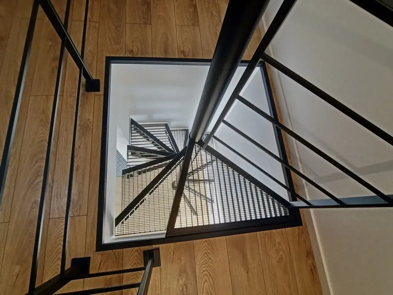 Nowoczesne schody wachlarzowe z metalową balustradą i drewnianą podłogą, prowadzące w dół.