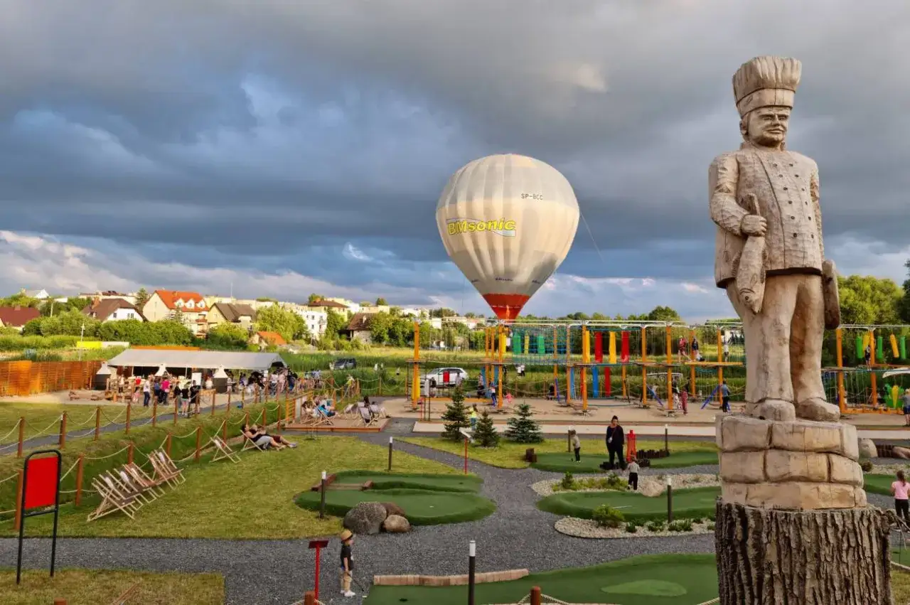 Drewniany rybak i balon na uwięzi zapowiadają świetne atrakcje Kaszuby dla dzieci: park linowy, mini golf i strefę relaksu.