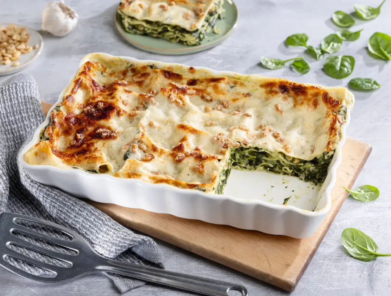 Herzhaftes Spinatlasagne-Rezept in einer Auflaufform, goldbraun &uuml;berbacken. Frische Spinatbl&auml;tter und Pinienkerne zieren die cremige Oberfl&auml;che.