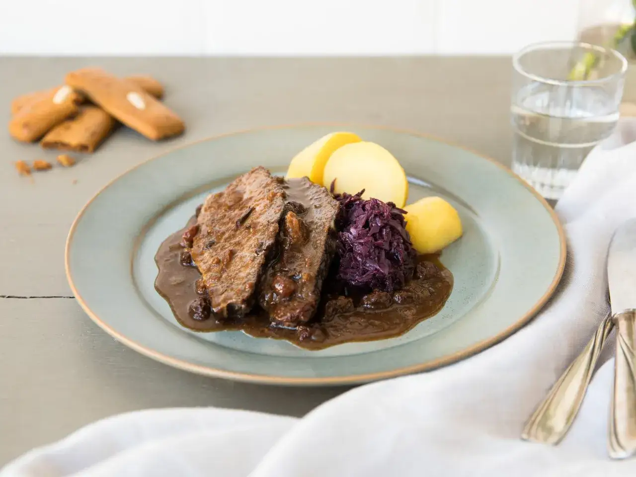 Herzhaftes Gulasch mit Rotkohl und Kartoffeln, ein Klassiker nach omas rezepte mittagessen. Dazu ein Glas Wasser und ein paar Kekse.