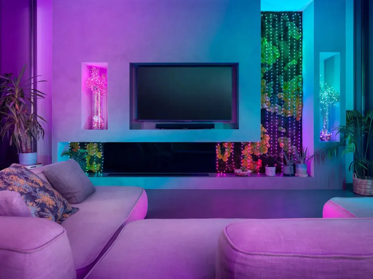 Un salon moderne aux lumières d'ambiance colorées. Le téléviseur est éteint, entouré de plantes et de guirlandes lumineuses. C'est quoi les lumens ? C'est la mesure de la lumière.