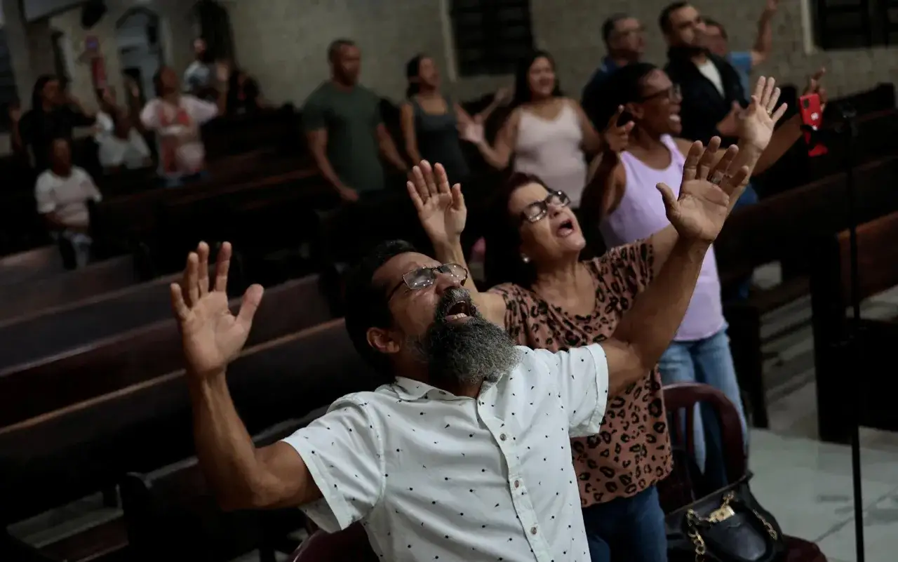 Menschen in einer Kirche mit erhobenen Händen, die sich an einer Predigt von Reinhard Hirtler erfreuen.
