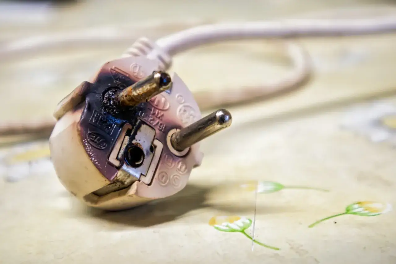 Angebrannter Stecker, der nach Kabelbrand riecht. Die Isolierung ist geschmolzen und die Kontakte sind stark verfärbt.