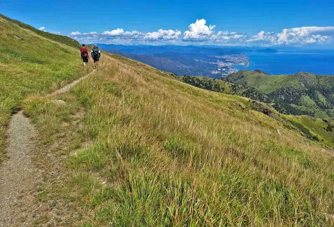 Escursionisti sul sentiero del **Passo del Faiallo**, con vista sul mare e sulla costa in lontananza.
