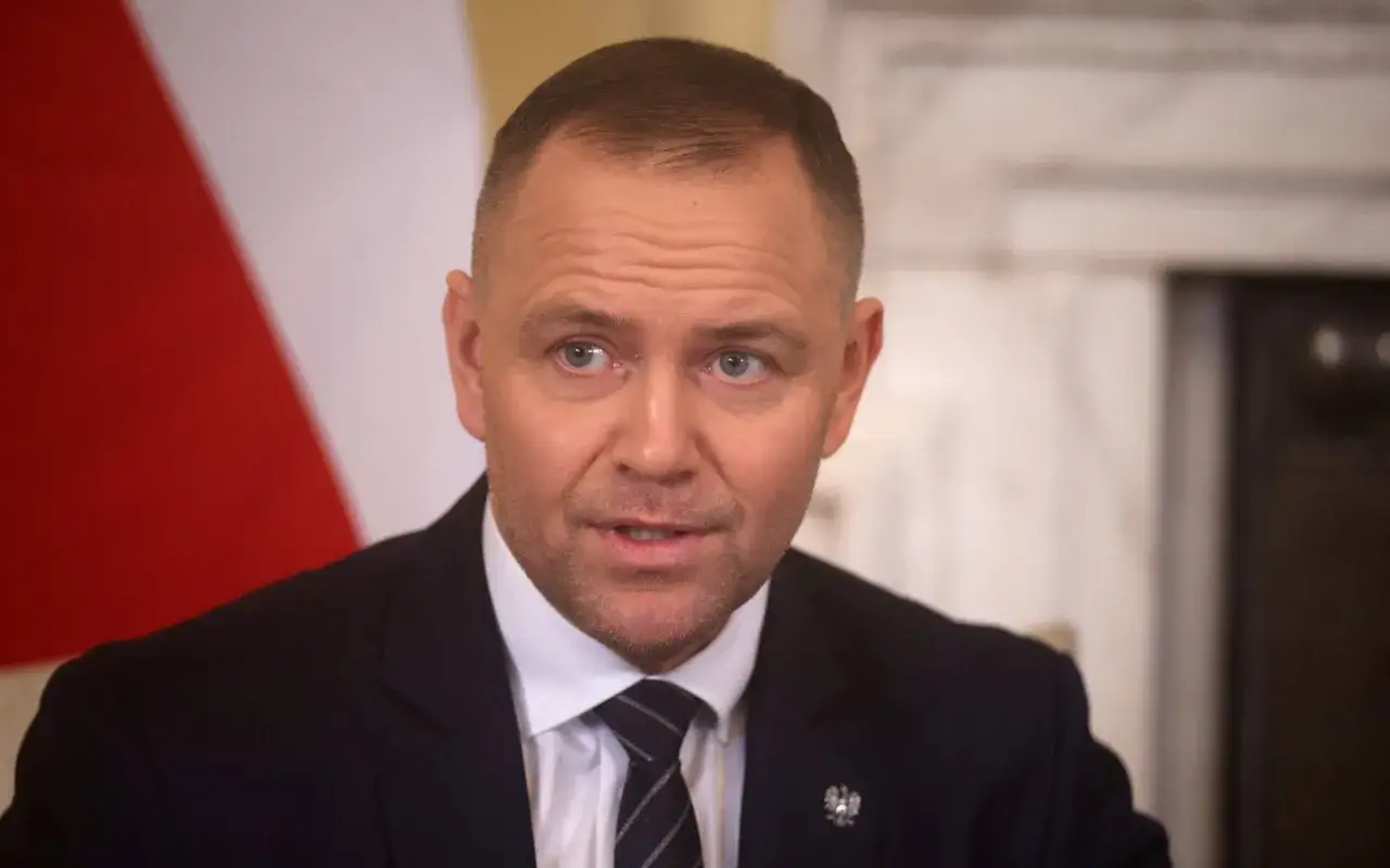Mężczyzna w garniturze, z flagą Polski w tle, zastanawia się, dlaczego prezydent nie skorzystał z prawa łaski wobec skazanych urzędników państwowych.