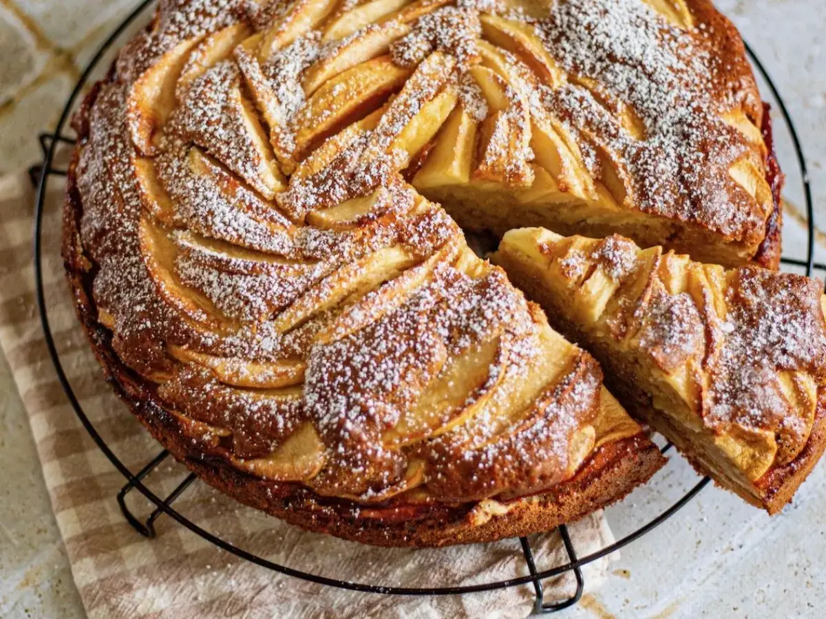 G&acirc;teau fondant aux pommes mascarpone, saupoudr&eacute; de sucre glace, avec une part coup&eacute;e.