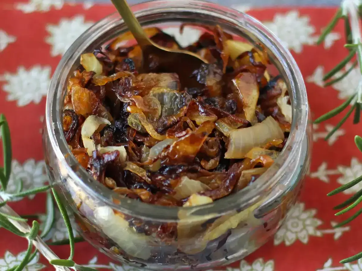 Un pot de confit d'oignons caramélisés, parfait pour savoir comment faire un confit d'oignons maison. Une cuillère dorée y est plongée.