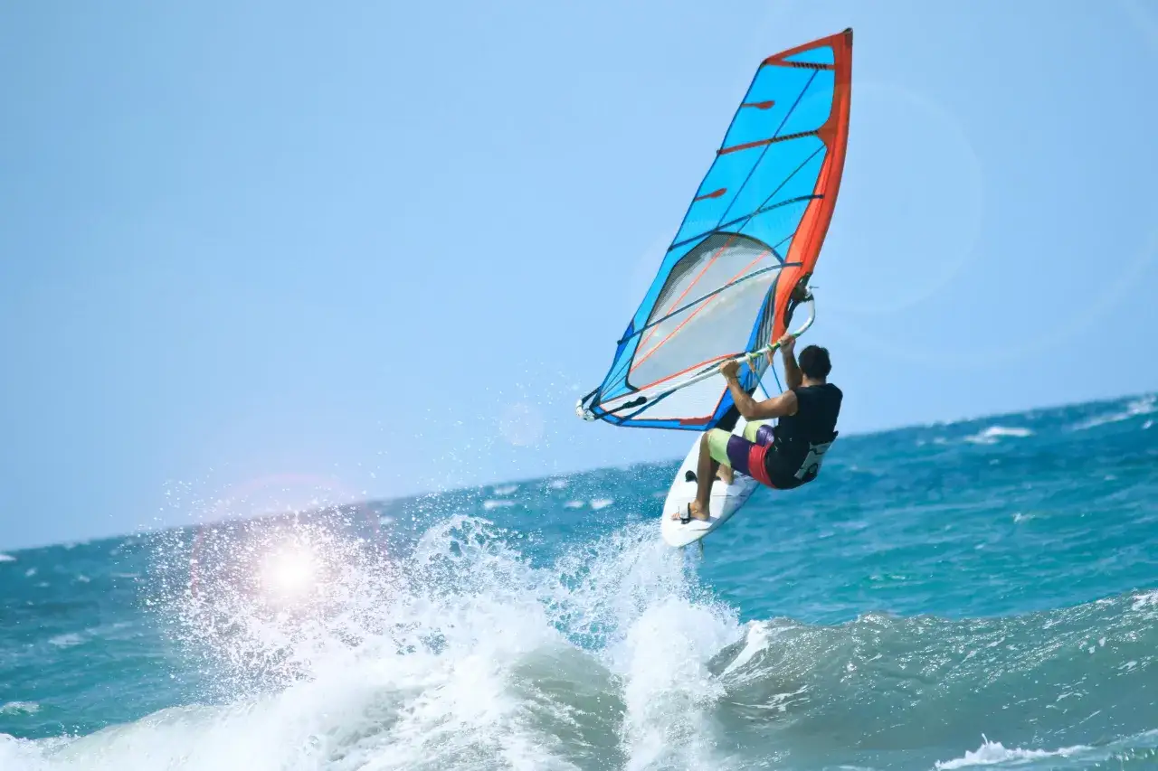 Ein Windsurfer springt über eine Welle im türkisfarbenen Meer. Das bunte Segel leuchtet in der Sonne. Ein perfekter Tag zum Windsurfen Kroatien!