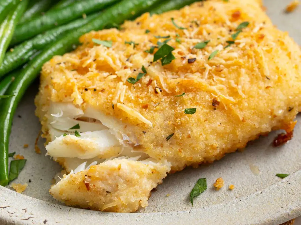Un délicieux filet d'aiglefin pané, prêt pour la cuisson, accompagné de haricots verts frais.