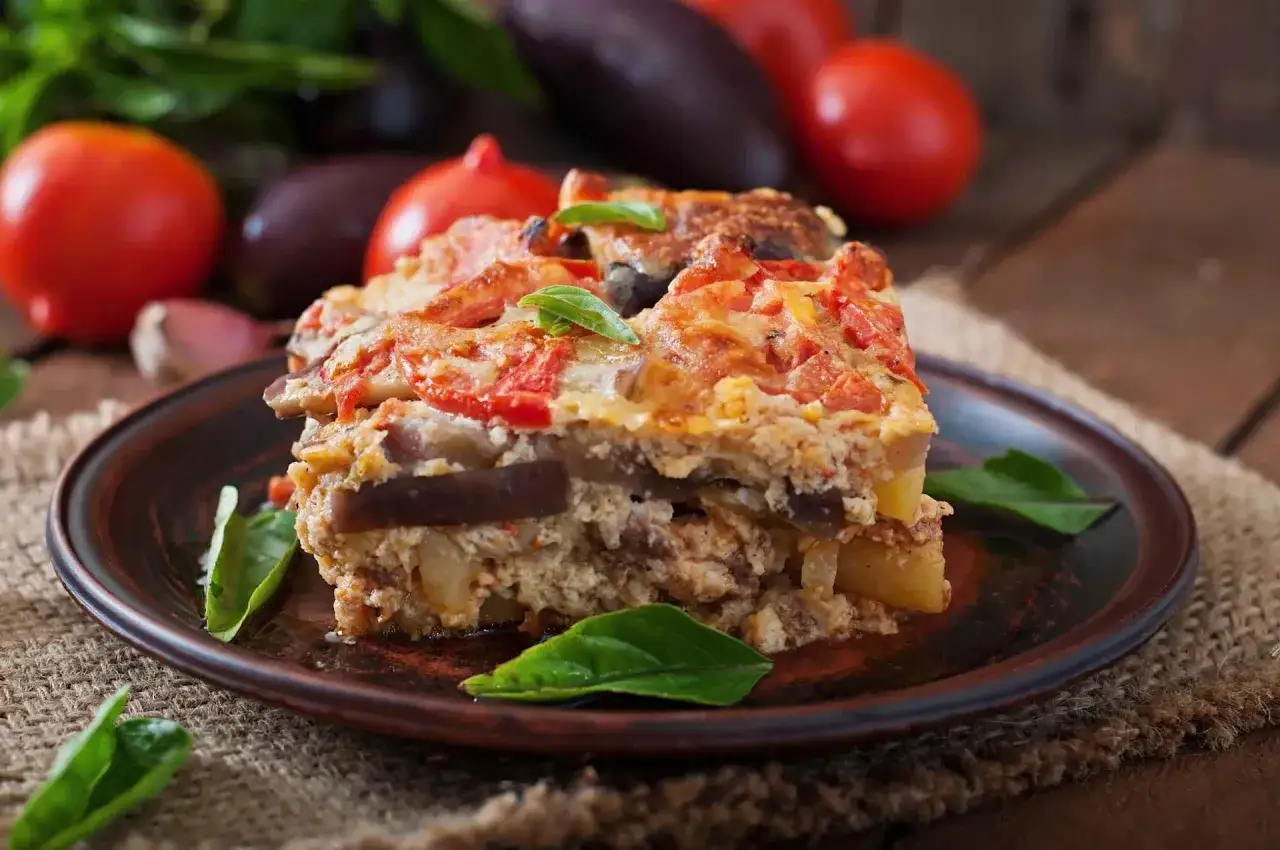 Un assaggio di cosa mangiare a Santorini: una deliziosa moussaka con melanzane, pomodoro e formaggio, guarnita con basilico fresco.