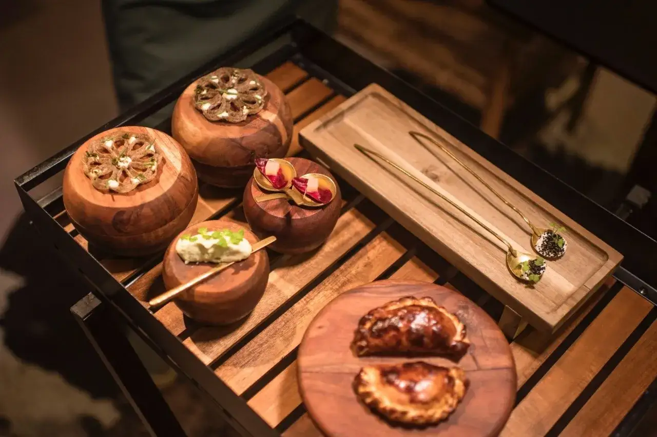 Deliciosos aperitivos presentados en cuencos de madera, como un solete Repsol, junto a empanadillas doradas y cucharas doradas con delicadas preparaciones.