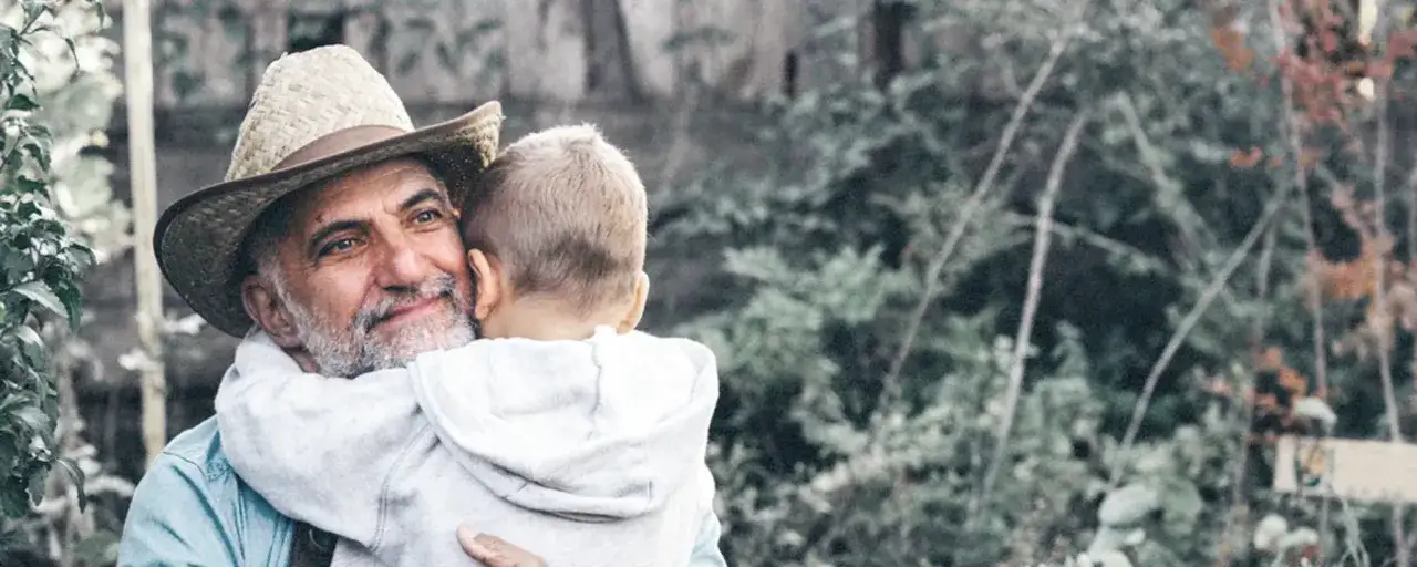 Ein Mann mit Strohhut umarmt ein Kind. Auch wenn das Kind bei der Oma lebt, ohne Sorgerecht, zeigt die Szene Liebe und Geborgenheit.