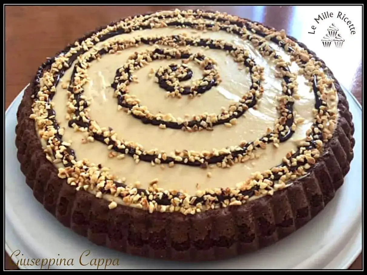 Torta alla Nutella con crema chiara, decorata con cioccolato e nocciole tritate. Un dolce invitante e goloso.