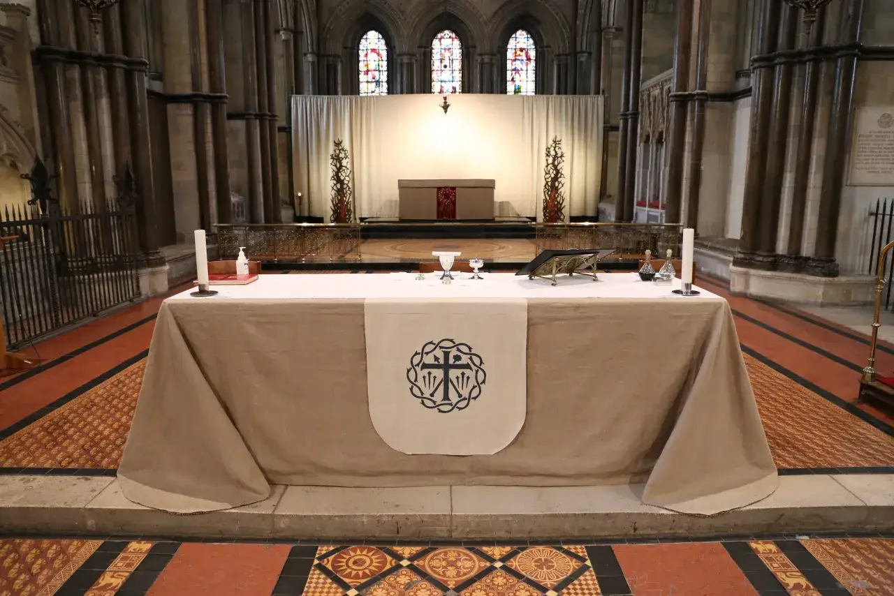 Altar set for Sunday in Lent, with a book, chalices, and candles. A banner with a cross symbol hangs from the altar cloth.