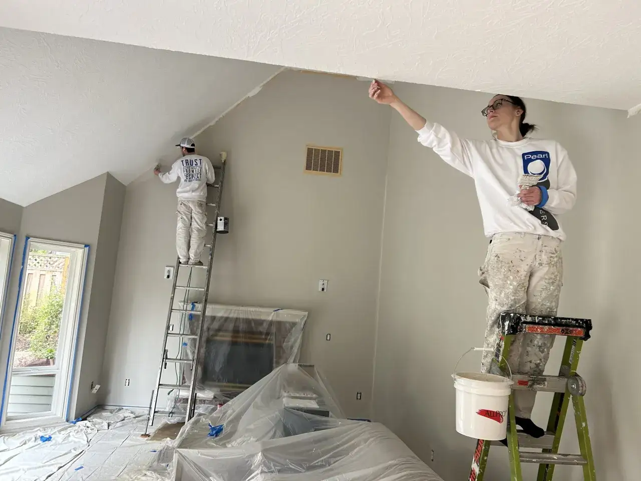Dos pintores trabajan en una habitaci&oacute;n, uno en una escalera alta y otro en una m&aacute;s baja. Ambos pintan el techo, respondiendo a la pregunta de si se pinta primero el techo o las paredes.