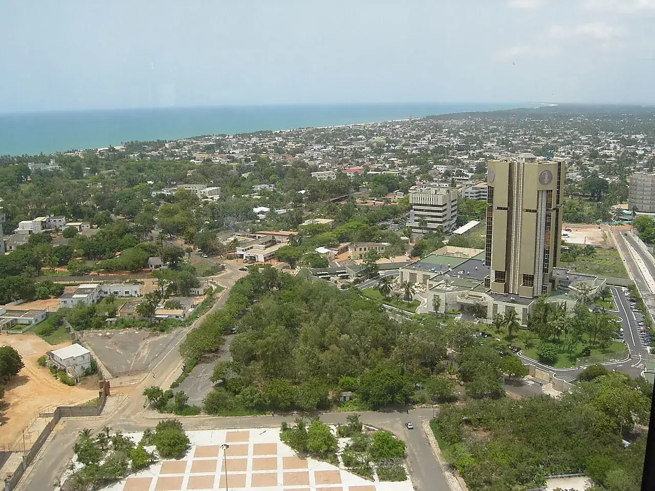 Widok na Lome, Togo, z dominującym złotym budynkiem banku i rozległym miastem w tle, nad błękitnym oceanem.