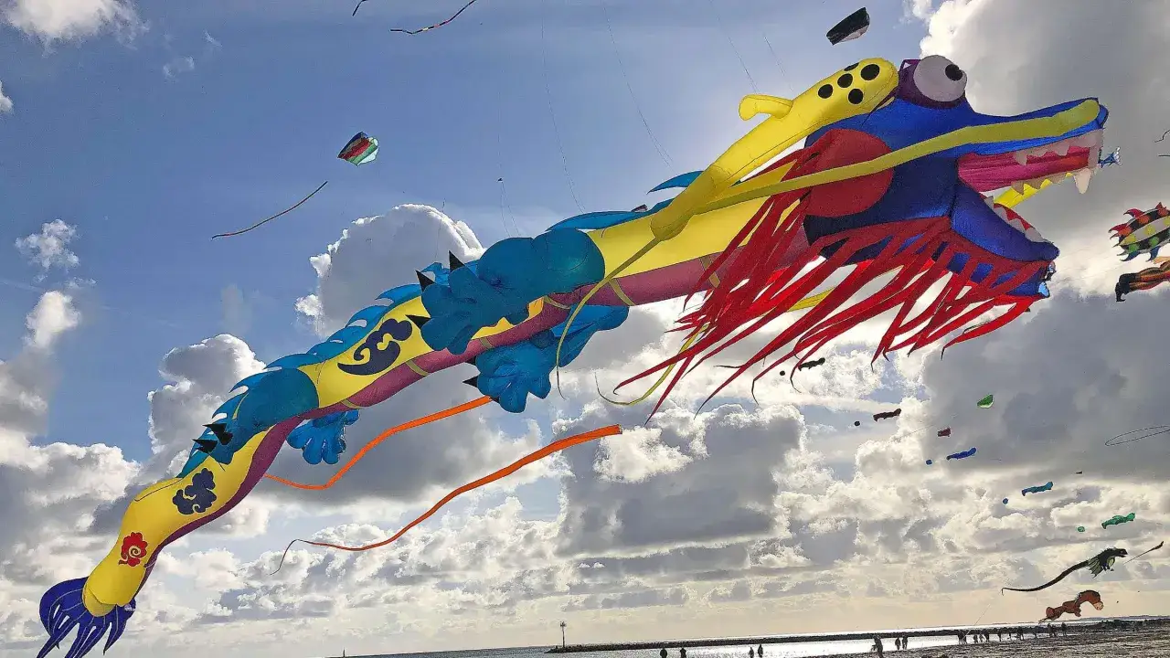 Ein riesiger, bunter Drachen fliegt beim Fehmarn Drachenfest über den Strand.