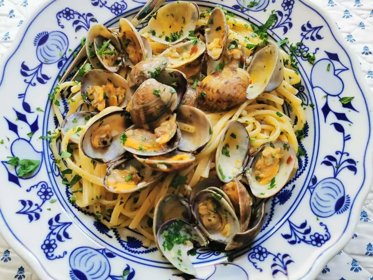 Pyszne spaghetti vongole z małżami i natką pietruszki na talerzu z niebieskimi wzorami.