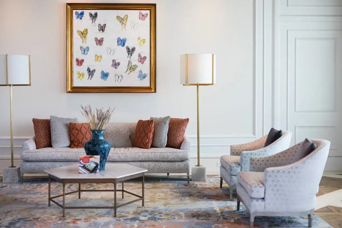 Salotto con divano e poltrone, un quadro di farfalle e un tavolino. Un mix di arredamento moderno e antico crea un ambiente accogliente.