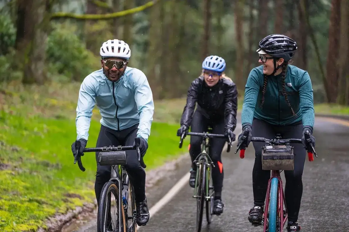 Trzech rowerzyst&oacute;w w kaskach jedzie po mokrej drodze. Warto mieć odpowiedni kask w g&oacute;ry, nawet gdy pada deszcz.