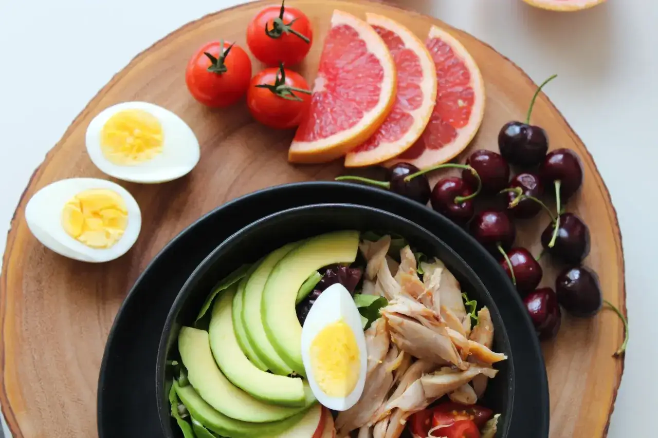 Sałatka z kurczakiem, awokado i jajkiem, idealna na dietę FODMAP. Na drewnianej desce pomidorki, grejpfrut i wiśnie.