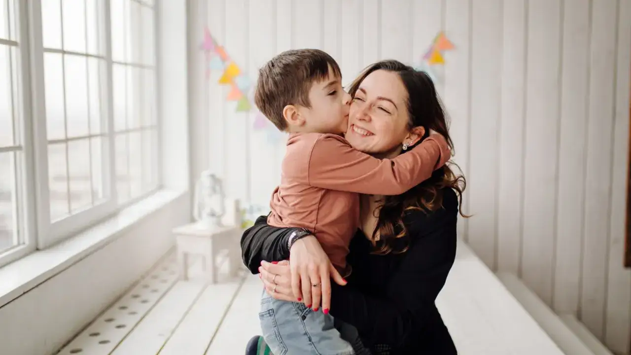 Un niño da un tierno beso a su madre, quien sonríe con orgullo. Un momento que inspira orgullosa frases cortas para un hijo varón.