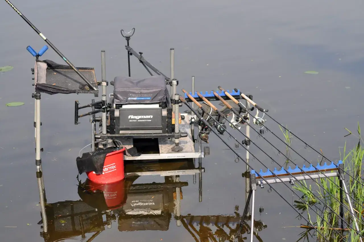 Gotowe stanowisko method feeder z kilkoma wędkami i czerwonym wiadrem, gotowe na połów.