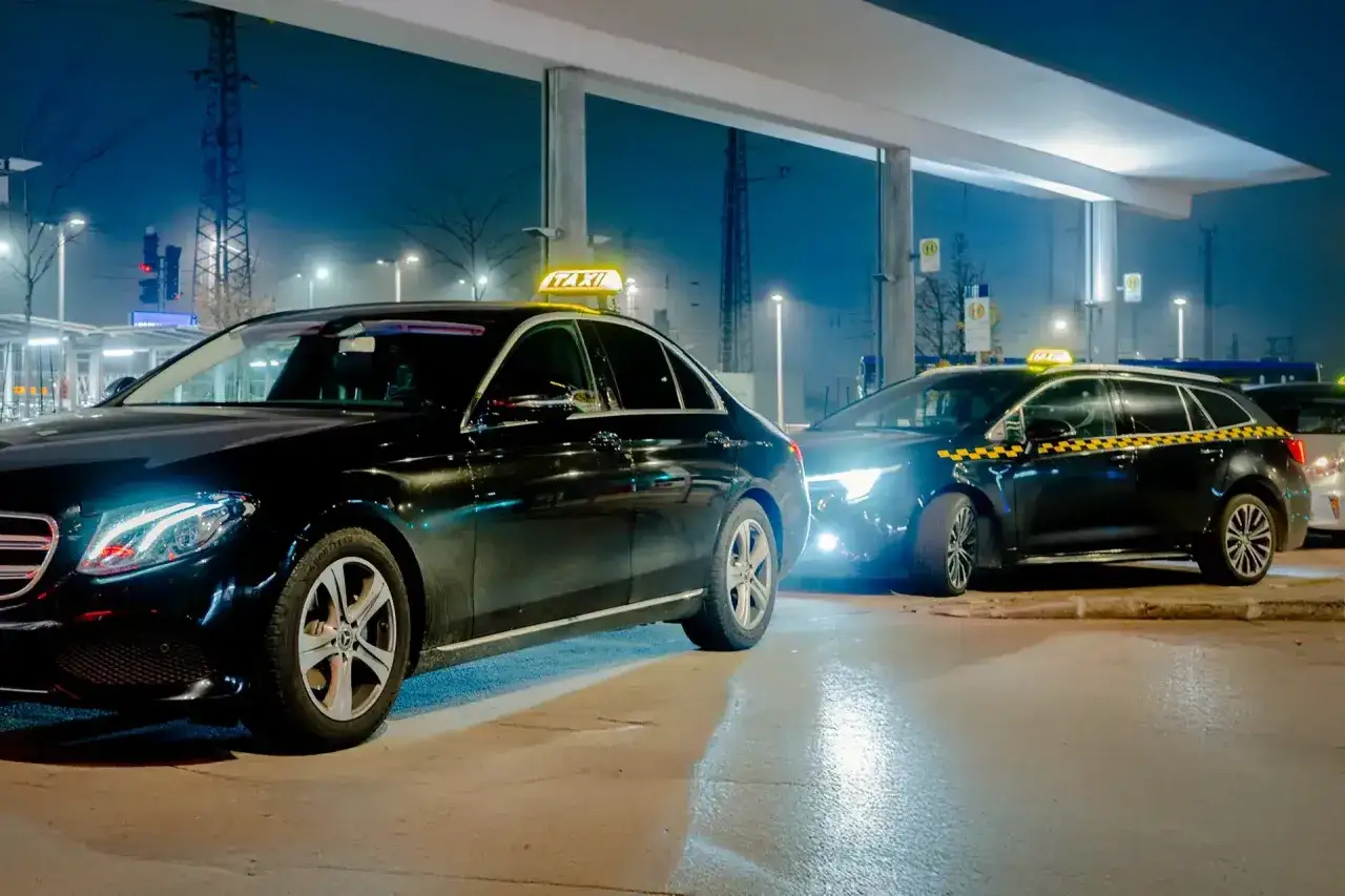 Schwarze Taxis warten im Dunkeln auf Passagiere. Ein beleuchteter Flughafen bei Nacht, mit Lichtern und Autos.