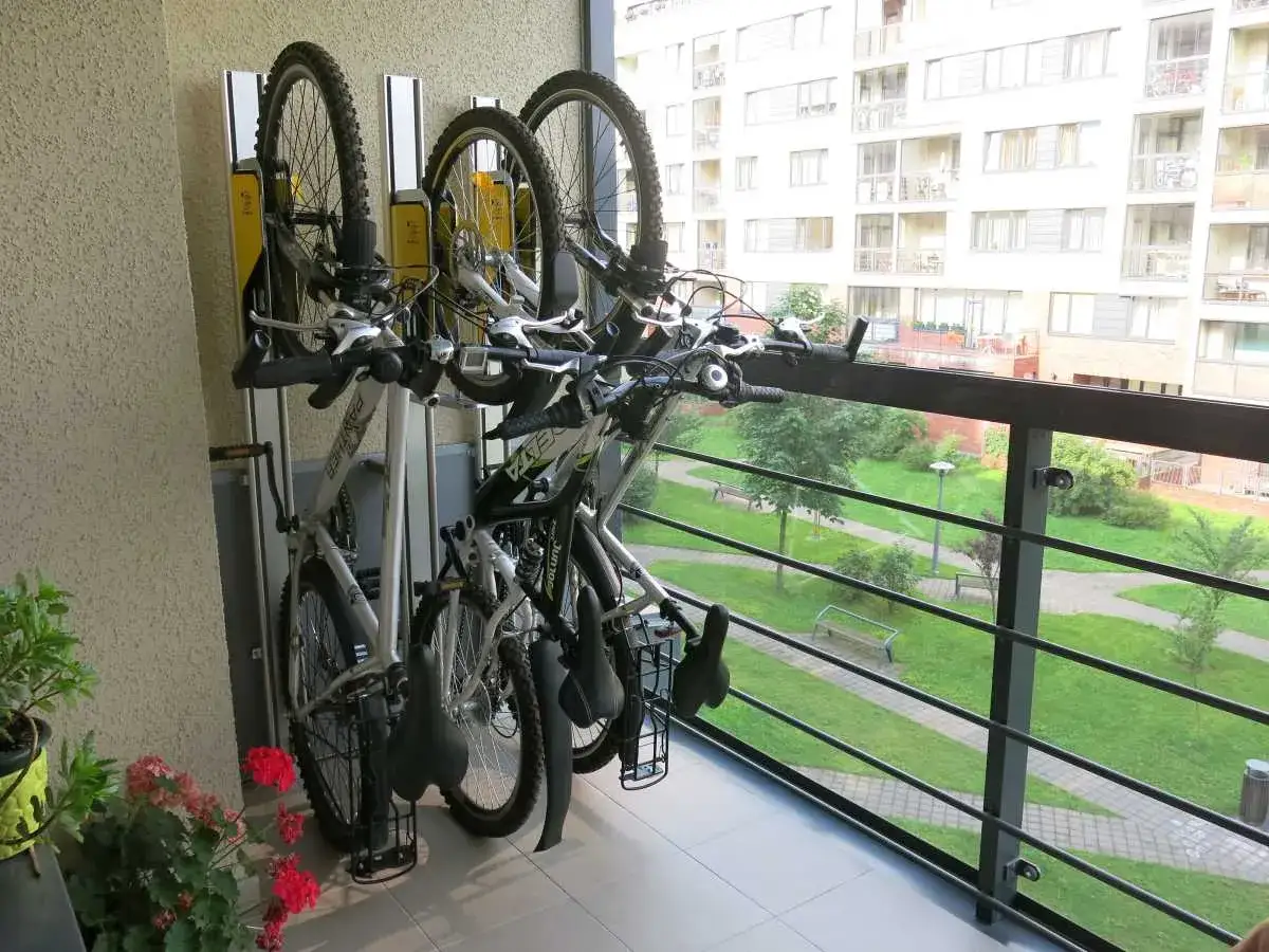 Pionowe przechowywanie roweru na balkonie. Trzy rowery stoją na stojaku, z widokiem na zielony dziedziniec i budynek mieszkalny.