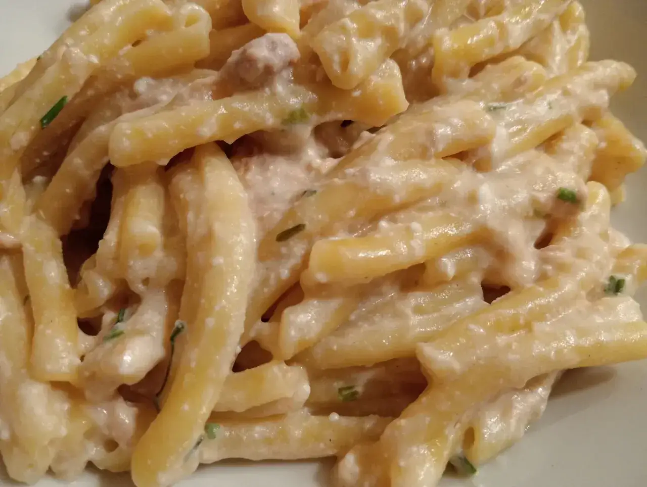 Pyszne makaron strozzapreti w kremowym sosie z kawałkami mięsa i zieloną posypką.