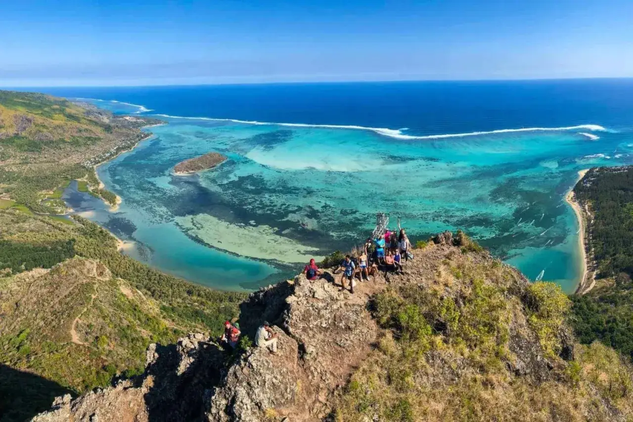 Gruppe von Wanderern genie&szlig;t atemberaubende Aussicht vom Gipfel des Le Morne Brabant auf t&uuml;rkisfarbene Lagunen und das weite Meer.