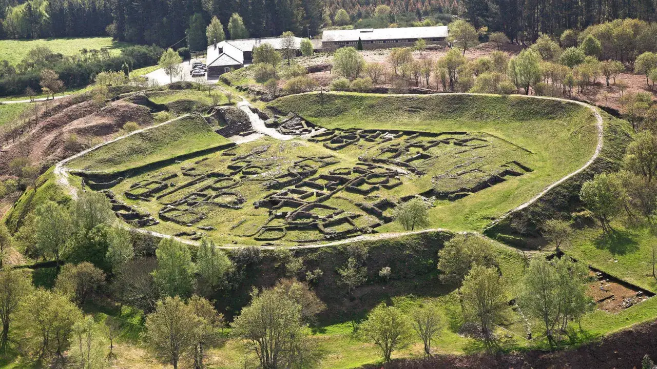 Vista aérea del castro de Viladonga, con sus murallas y restos de edificaciones circulares y rectangulares, rodeado de vegetación.
