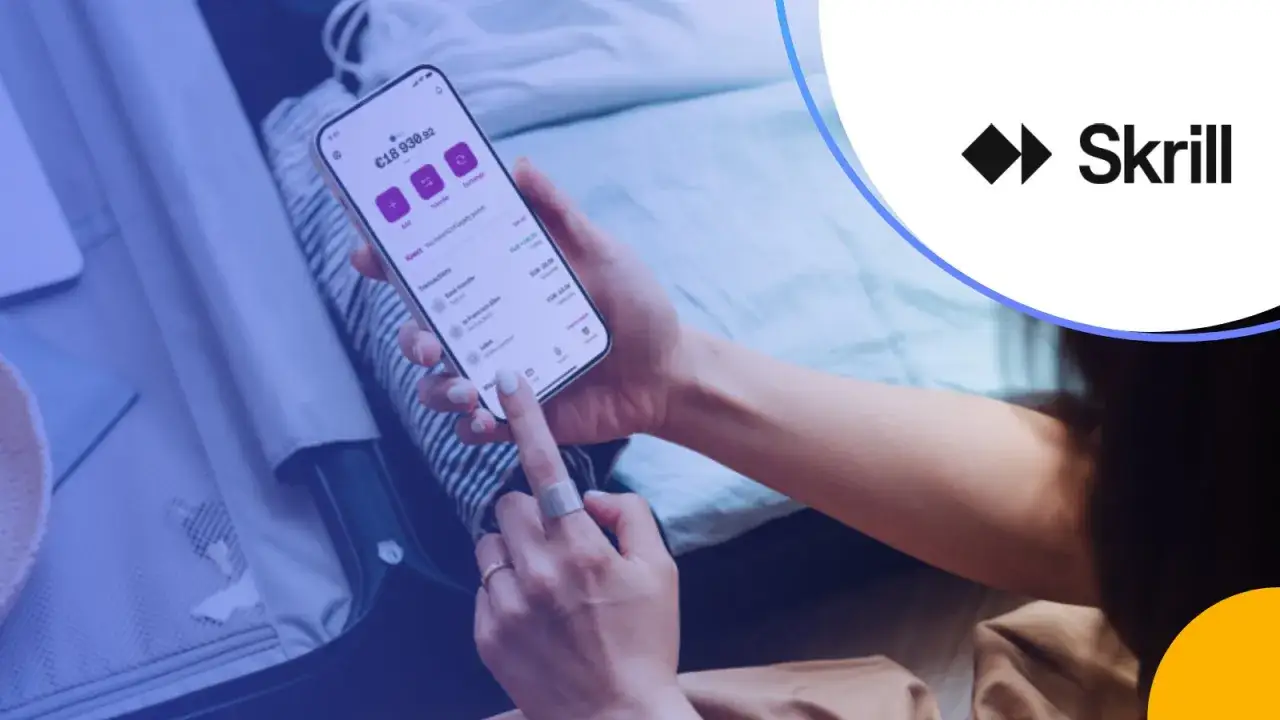 Dłoń trzyma smartfon z aplikacją Skrill, pokazującą saldo i transakcje. To dowód, co to Skrill – szybkie płatności online.