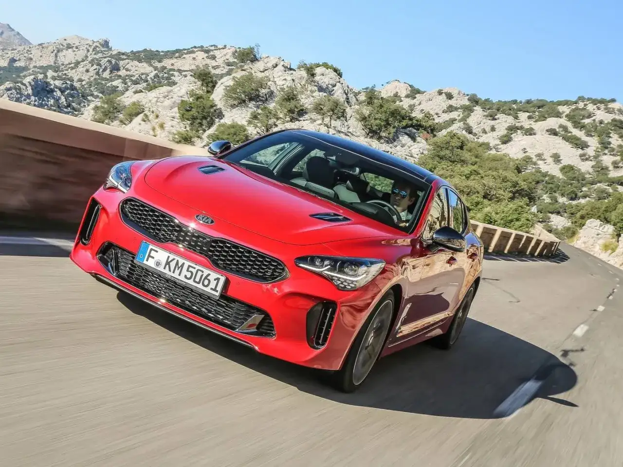Un Kia Stinger GT CV rojo serpentea por una carretera montañosa, con el sol brillando y el conductor disfrutando del viaje.