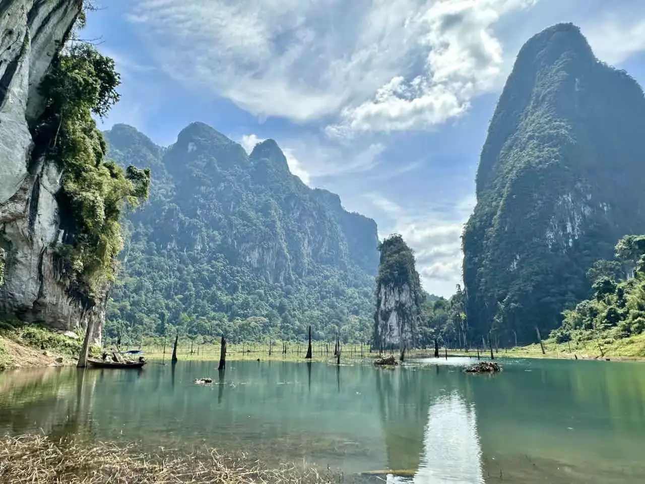 Khao Sok Nationalpark: Majest&auml;tische Karstfelsen ragen aus einem ruhigen See, umgeben von &uuml;ppigem Dschungel. Ein Boot gleitet &uuml;ber das Wasser.