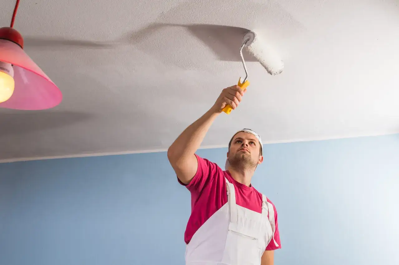 Un peintre en salopette blanche et t-shirt rose peint un plafond. Il utilise un rouleau jaune. Combien de temps pour peindre un plafond de 50m2 ?