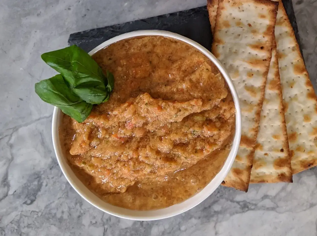Ein cremiger Tomatendip, perfekt f&uuml;r Ihr n&auml;chstes Tomatendip Rezept, garniert mit frischem Basilikum und serviert mit knusprigen Crackern.