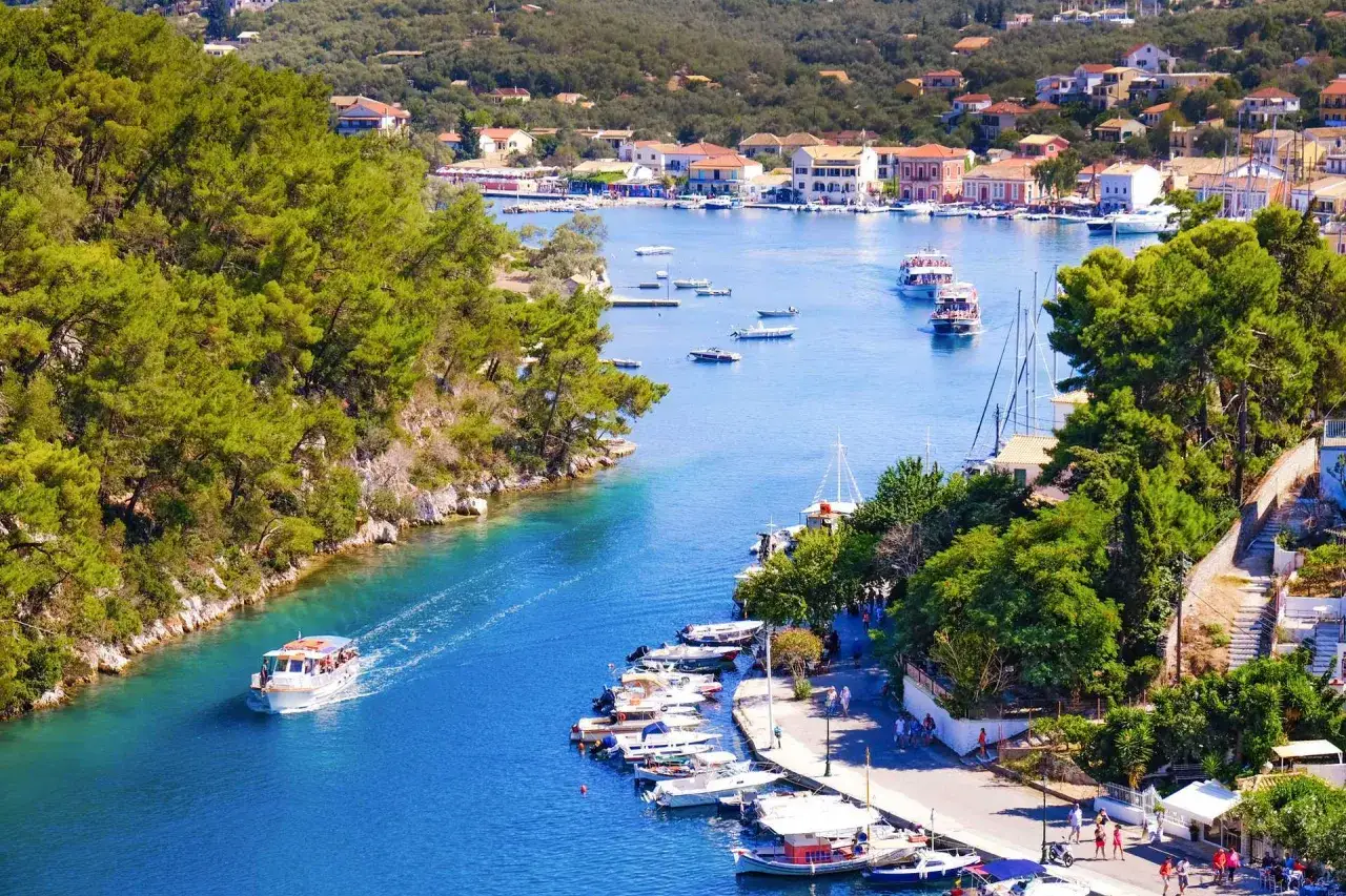 En båt färdas på det turkosblå vattnet i Paxos, Grekland, omgiven av grönska och charmiga hus.