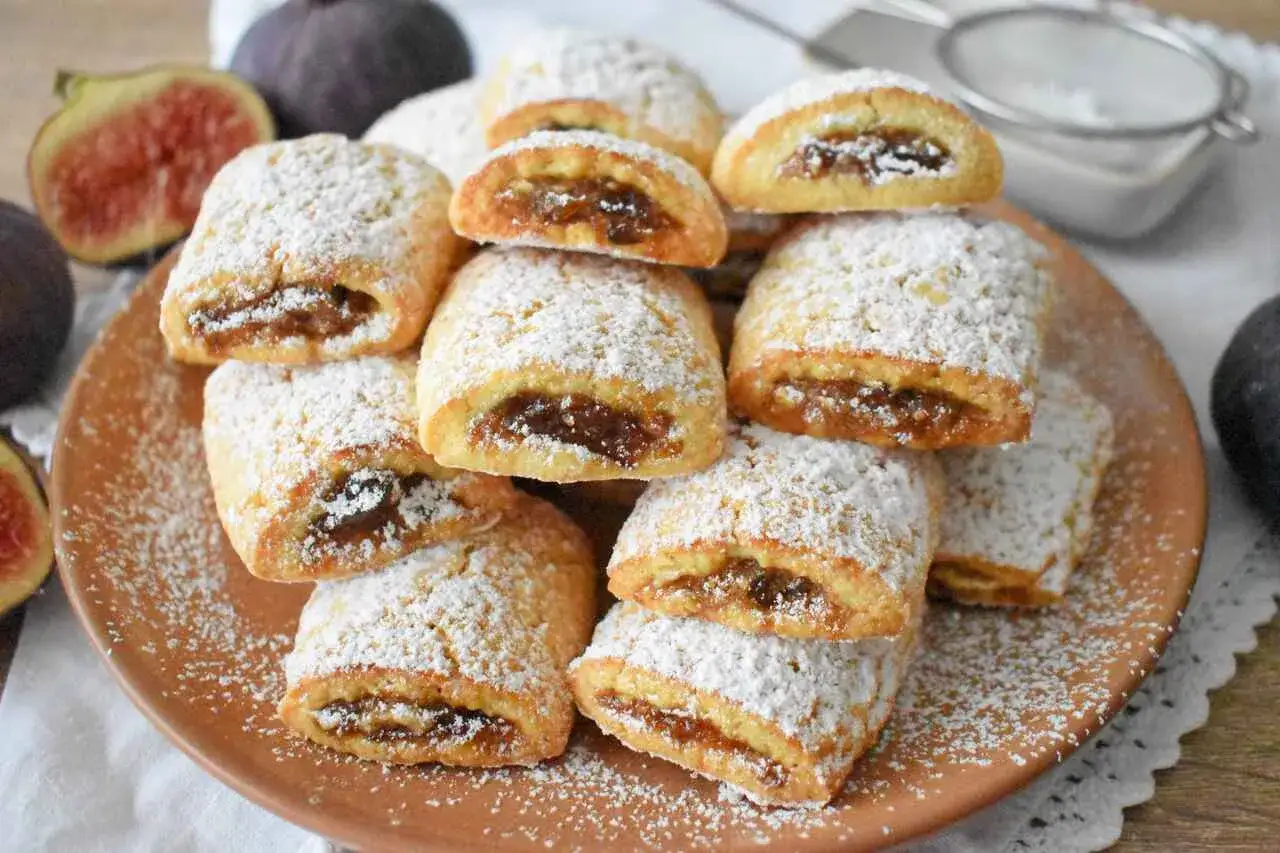 Stos ciasteczek włoskich z figami, posypanych cukrem pudrem, obok świeżych fig.