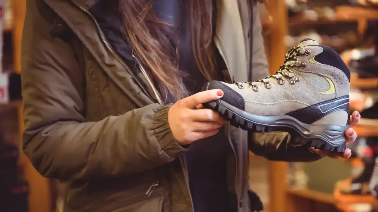 A person in a green jacket holds a hiking boot, wondering, 